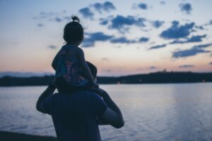 père porte sa fille sur les épaules devant un lac après un test adn