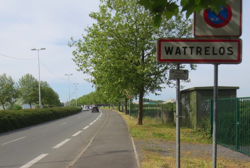 Panneau de signalisation d'entrée de ville indiquant Wattrelos au bord d'une route bordée d'arbres.