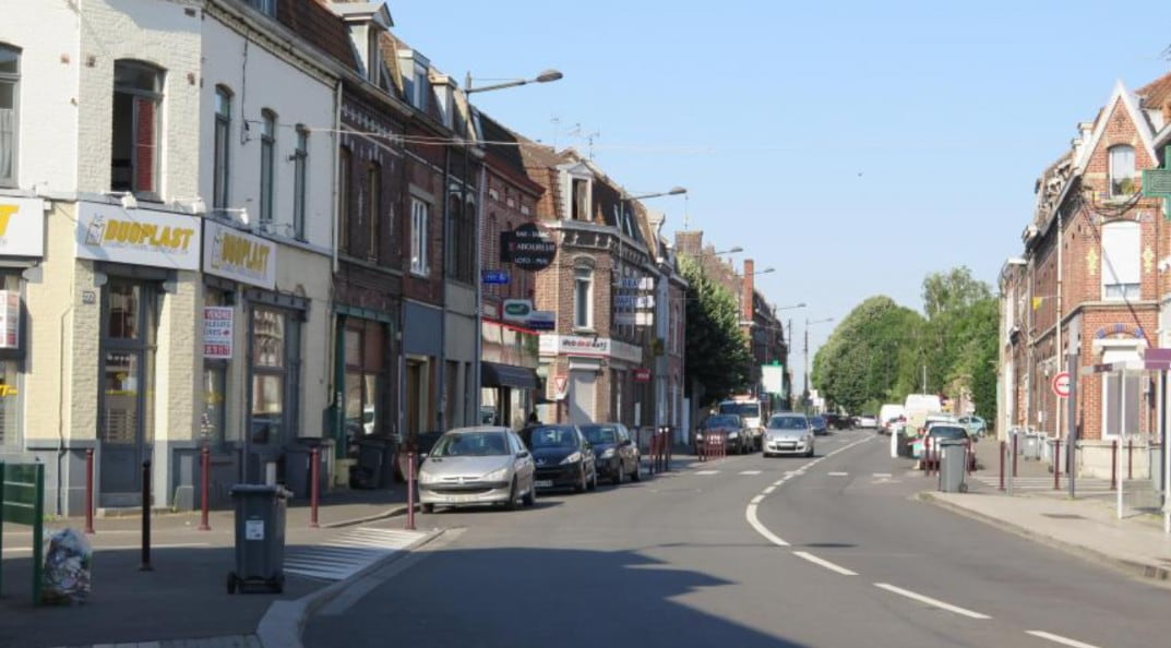 Vue d'une rue commerçante bordée de maisons traditionnelles en briques à Wattrelos sous un ciel dégagé.